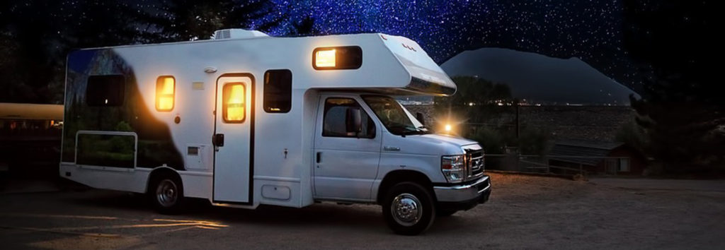 Camping-car à capucine blanc stationné de nuit sous un ciel étoilé, fenêtres éclairées