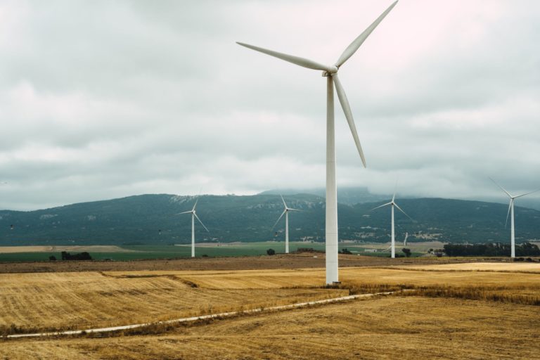 Éoliennes blanches dans un paysage de champs et de collines sous un ciel nuageux