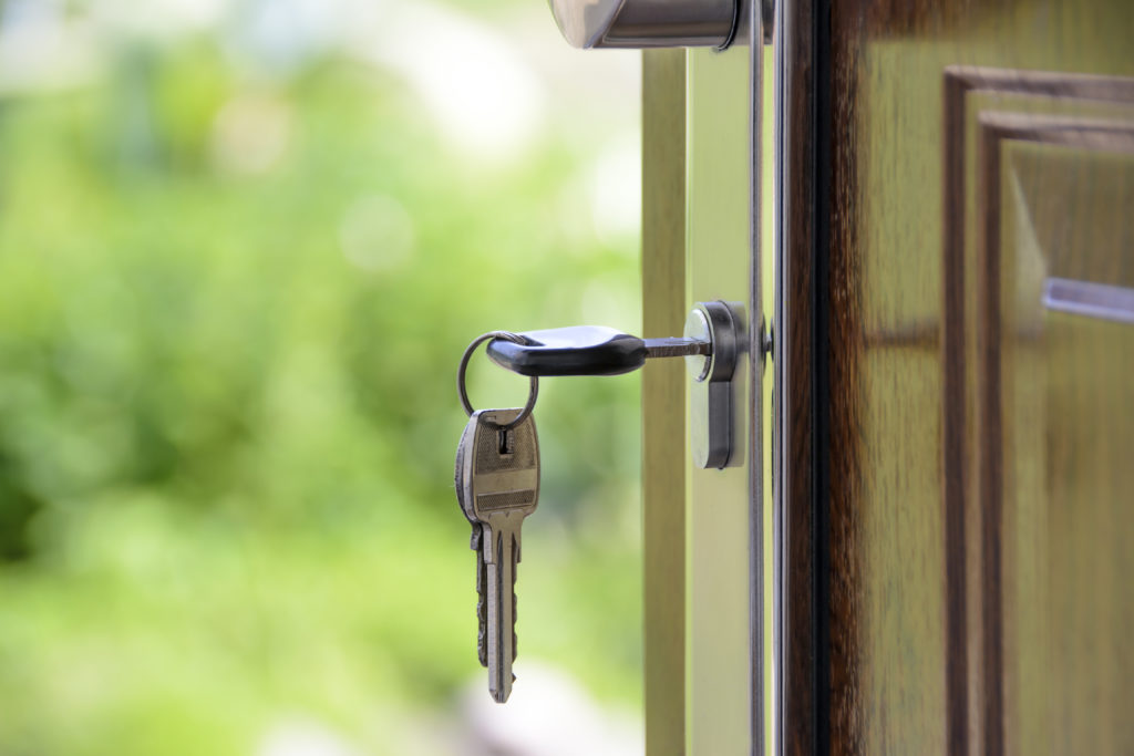 Clé insérée dans la serrure de la porte d’entrée en bois d’une maison, jardin flou en arrière-plan