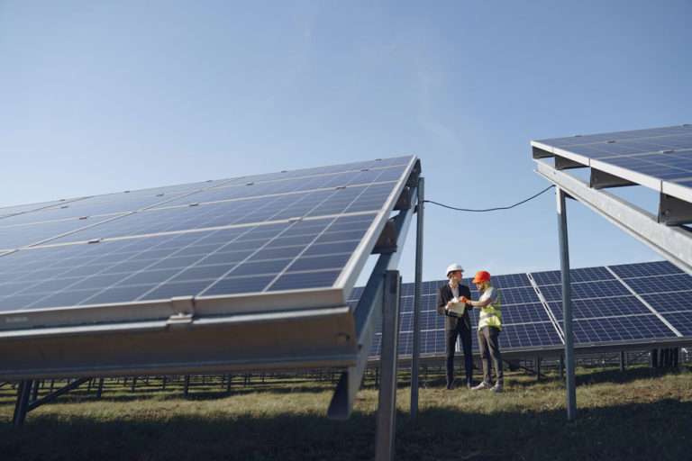 Deux personnes casquées, dont une en gilet de sécurité, discutent entre des rangées de panneaux photovoltaïques posés au sol