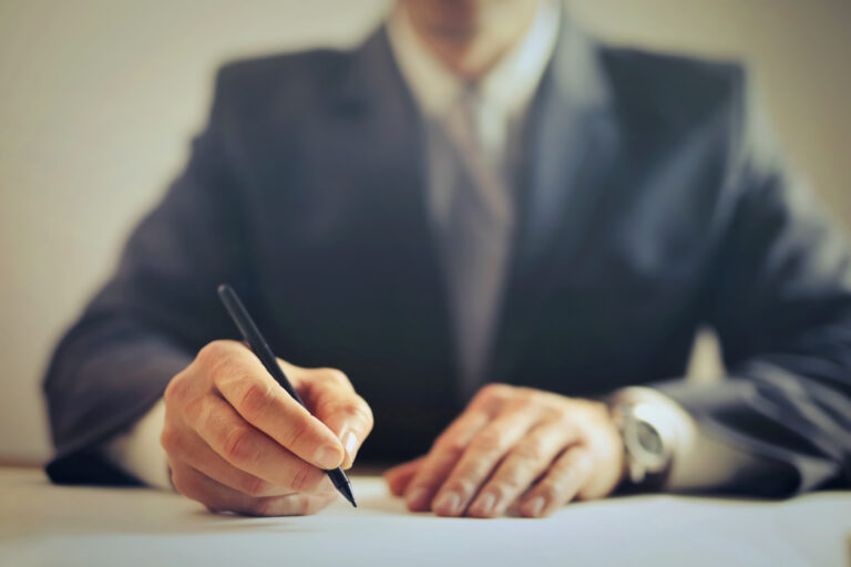 Personne en costume qui signe un document posé sur un bureau