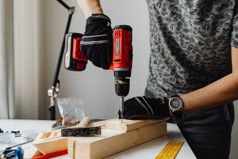Personne qui perce une planche de bois avec une visseuse sans fil sur un plan de travail